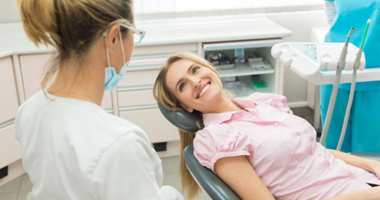 Young, blonde-haired woman smiling at a dental professional during a visit
